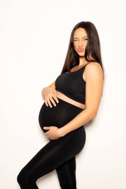 Siyah taytla poz veren hamile bir genç kadın ve beyaz arka planda bir gömlek.