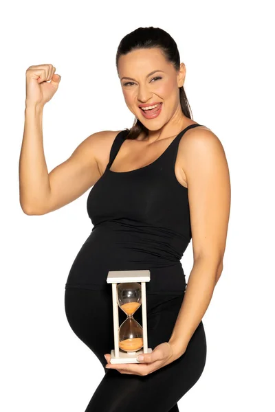 妊娠中の若い幸せな女性黒のレギンスとシャツ白い背景に砂時計でポーズ — ストック写真