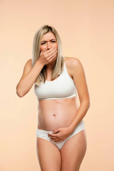 Mujer Embarazada Joven Lencería Disgustada Sufriendo Náuseas Sobre Fondo Beige — Foto de Stock