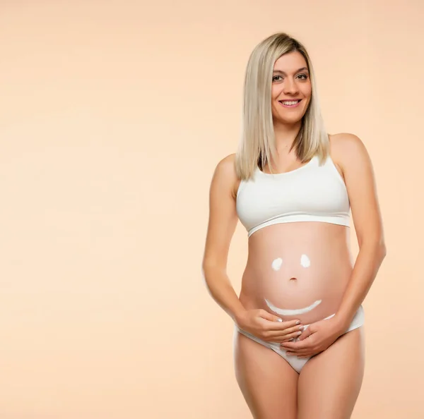 未来的母亲面带微笑地摆姿势 用米色背景在肚子上画画 — 图库照片