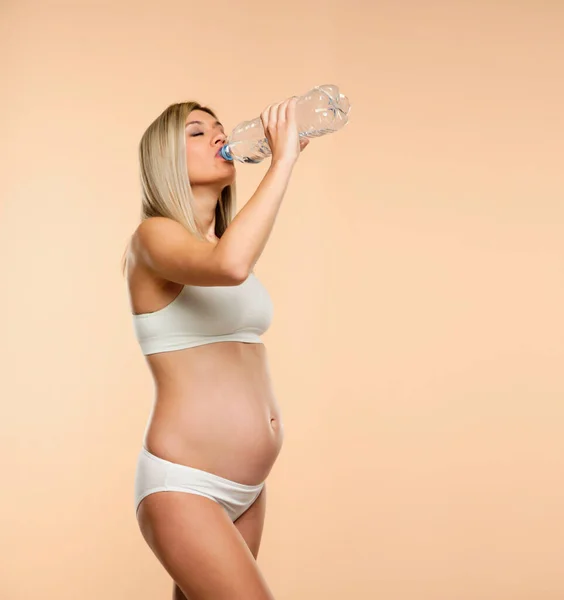 穿着内衣的年轻貌美的女人从米色背景的塑料瓶里喝水 — 图库照片
