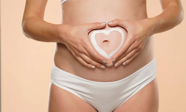 Kobieta Ciąży Robi Kształt Serca Rękami Nad Brzuchem Beżowym Tle — Zdjęcie stockowe