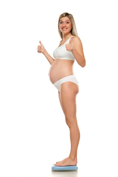 年轻快乐的孕妇站在白色背景的天平上 — 图库照片