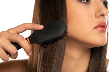 Genç bir kızın beyaz arka planda düz, uzun saçlarını taramasına yakından bakın.