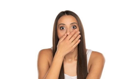 Şok olmuş genç bir kadın ellerini beyaz arka planda tutarak ağzını kapatıyor.