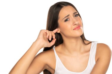 Kulağım kaşınıyor. Kızgınlık duyguları olan beyaz arka planda genç bir kadın parmağıyla kulağını kaşıyor.