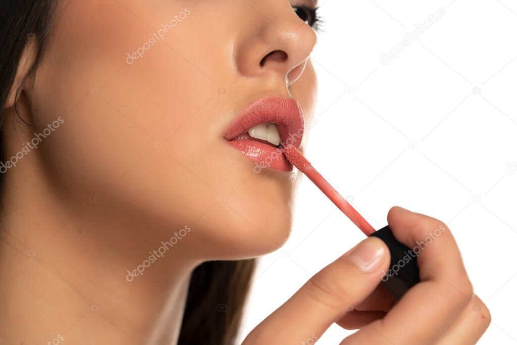 Closeup of woman applying a lip gloss on her lips on a white background