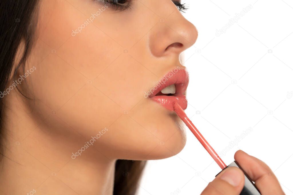 Closeup of woman applying a lip gloss on her lips on a white background