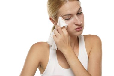 Genç ciddi sarışın kadın beyaz arka planda ıslak mendille yüzünü temizliyor.