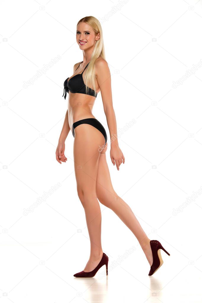 Young smiling blond woman walking in swimsuit on a white background