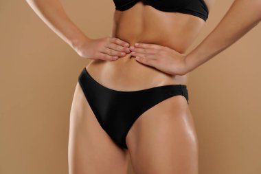 İnce bir kadın, elleri bej arka planda ince belini tutuyor.