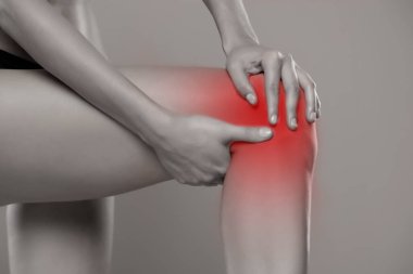 Kadın ağrıyan dizini gri arka planda tutuyor.