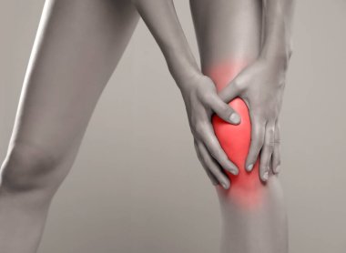 Kadın ağrıyan dizini gri arka planda tutuyor.