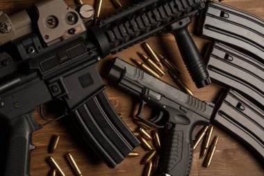 Optik görüşlü m4 tüfeği, el tabancası, mühimmat ve mermiler ahşap masada.