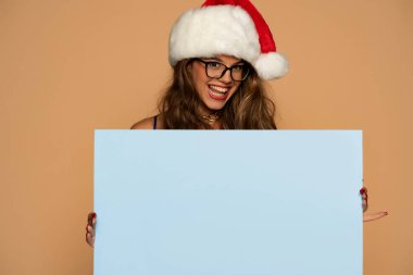 Noel, Noel, Noel, insanlar, reklam, satış konsepti - mavi elbiseli mutlu kadın ve bej arka planda boş mavi panelli Noel Baba yardımcısı şapkası