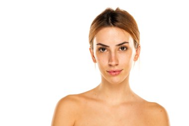 Stüdyoda beyaz bir arka planda makyajsız ve saçları bağlanmış ciddi bir genç kadının portresi.