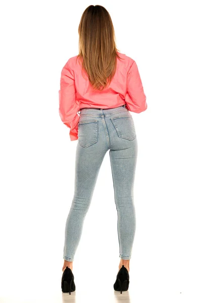 白い背景にピンクのシャツと青いジーンズでスタジオでポーズをとる若い女性の背面図 — ストック写真