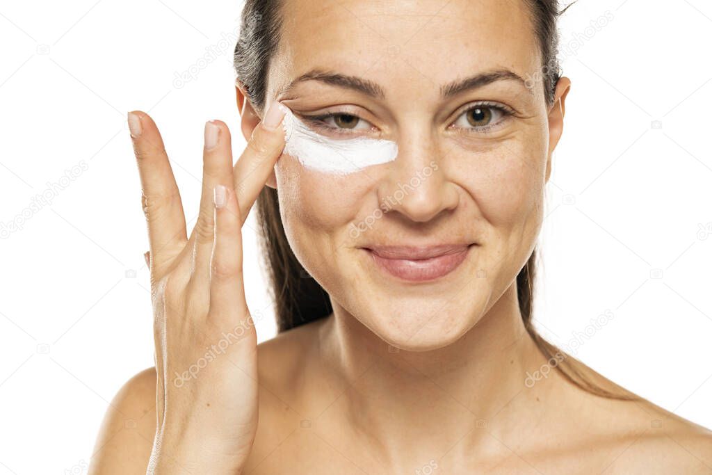 young woman apply cosmetic product under the eye on a white background