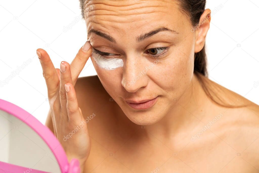 young woman apply cosmetic product under the eye on a white background