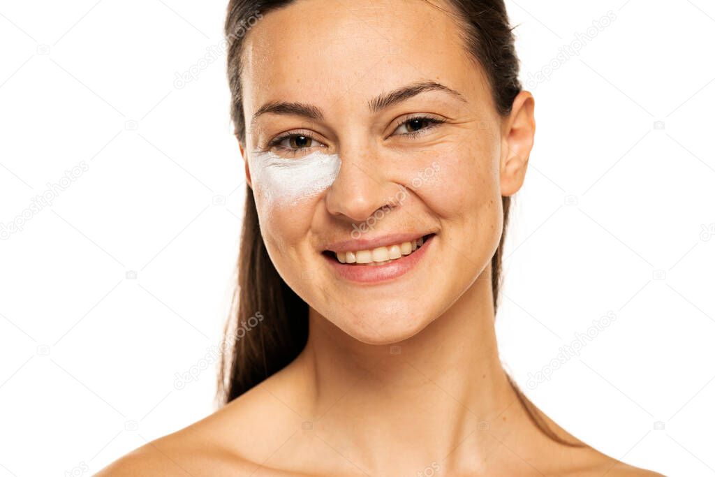 Portrait of a young woman with cosmetic product under the eye on a white background.