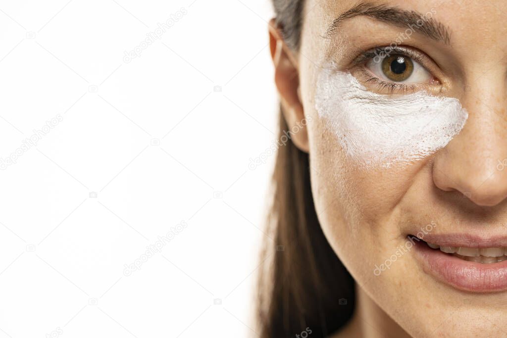 Half postrait of a young woman with cosmetic product under the eye on a white background