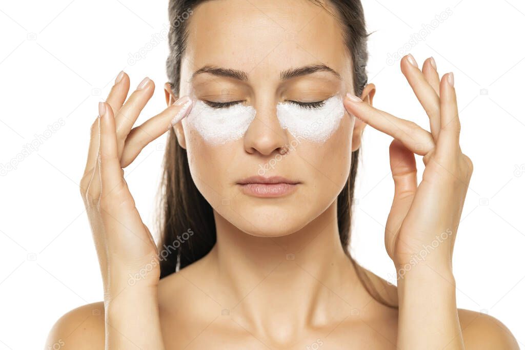 young woman apply cosmetic product under the eyes on a white background