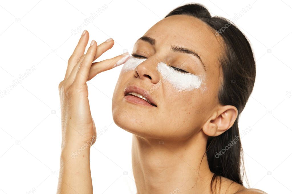 young woman apply cosmetic product under the eyes on a white background