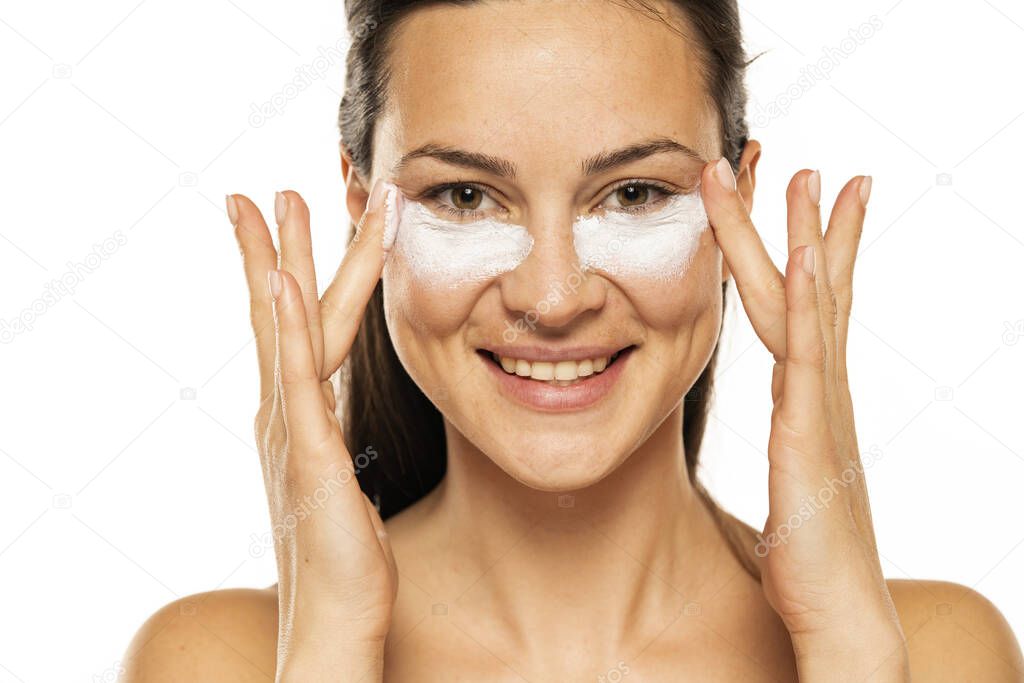 young happy  woman apply cosmetic product under the eyes on a white background