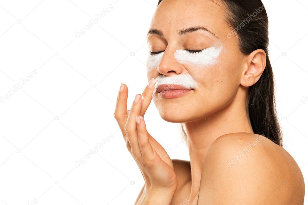 young woman apply cosmetic product under the eyes and nose on a white background