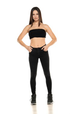 Siyah kotlu ve kısa bluzlu genç bir kadının beyaz arka planda poz verişi.