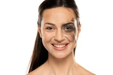 Yüzü kirli ve makyajsız gülümseyen genç bir kadın beyaz arka planda..