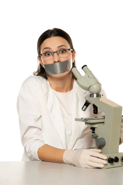 用显微镜描绘出困惑的女科学家的形象 并用白色背景贴在她的嘴上 — 图库照片