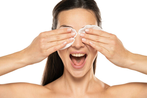 A young happy woman removing makeup with the cotton pads on white background