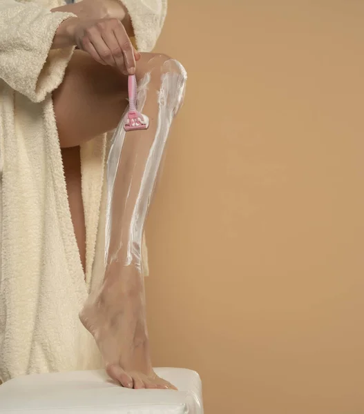 ベージュ地に足を剃る若い女性の切り取られたショット — ストック写真