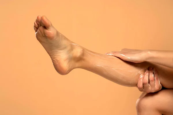 对于柔软的皮肤 用米色背景的润肤乳膏在女性腿上贴合 — 图库照片