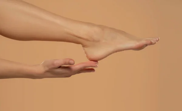脚后跟护肤 妇女用手触摸健康的脚体 腿脱离米色背景 — 图库照片