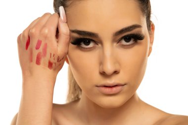 Beyaz bir arka planda elinde ruj ve dudak kalemi örnekleri gösteren genç bir kadın.