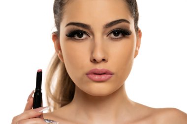 Beyaz bir arka planda ruj tutan güzel, ciddi bir genç kadının portresi.