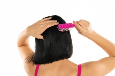 Beyaz arka planda siyah düz saçlarını tarayan bir kadın.