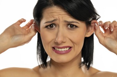 Güzel genç bir kadın beyaz arka planda parmaklarıyla kulaklarını çekiyor.