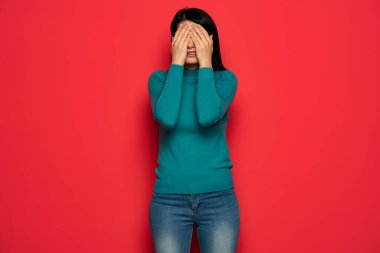 young woman covering her eyes with her hand palms on red background