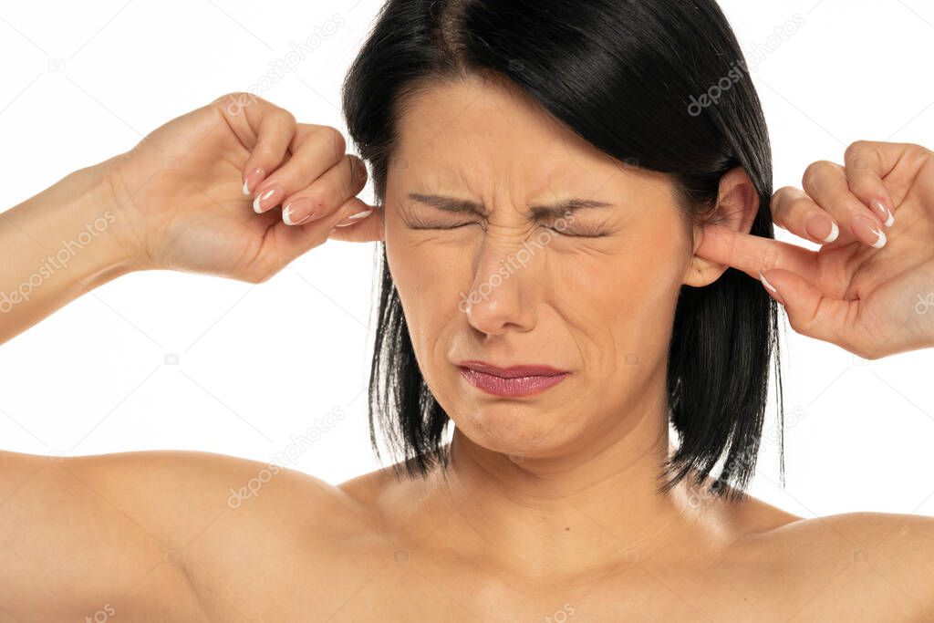 Portrait of disturbed young woman shouting while putting fingers on the ears on white background