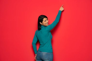 Kısa siyah saçlı, gülümseyen, sağ tarafını gösteren ya da kırmızı üzerine izole edilmiş bir kadın.