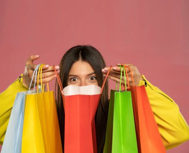 Young happy woman peeking over her shopping bags on a pink background