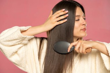 .Young woman enjoying brushing healthy hair on a pink background.