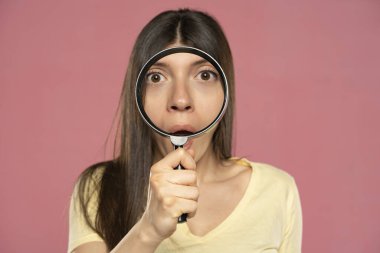 Pembe arka planda büyüteçten bakan genç bir kadının yakın plan portresi.