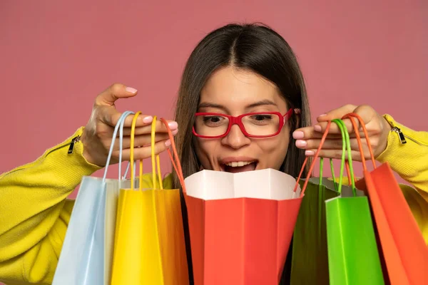 Young Happy Woman Peeking Her Shopping Bags Pink Background — стоковое фото
