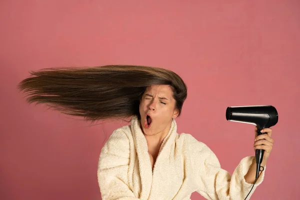 一个奇怪的女人用粉红背景的电扇擦干她的长发 — 图库照片