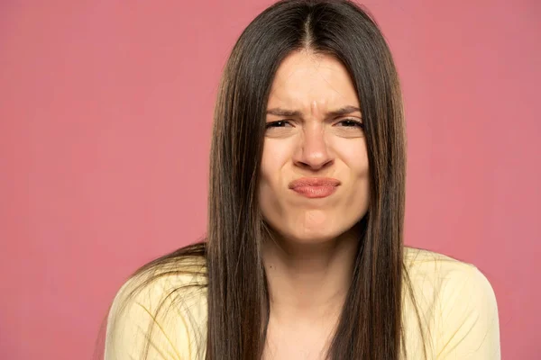 Uncertain young brunette woman with sour face on a pink background