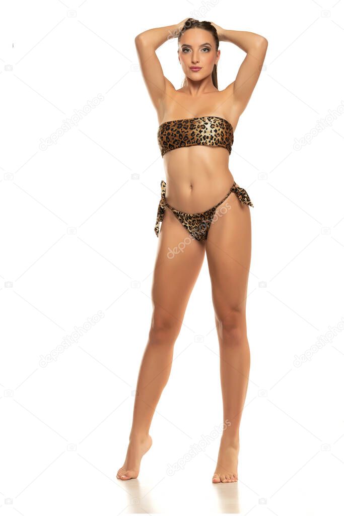 Young woman in leopard pattern bikini standing on a white background.
